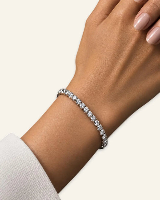 Woman wearing a silver-tone crystal tennis bracelet paired with a white cuff sleeve on a light cream background.