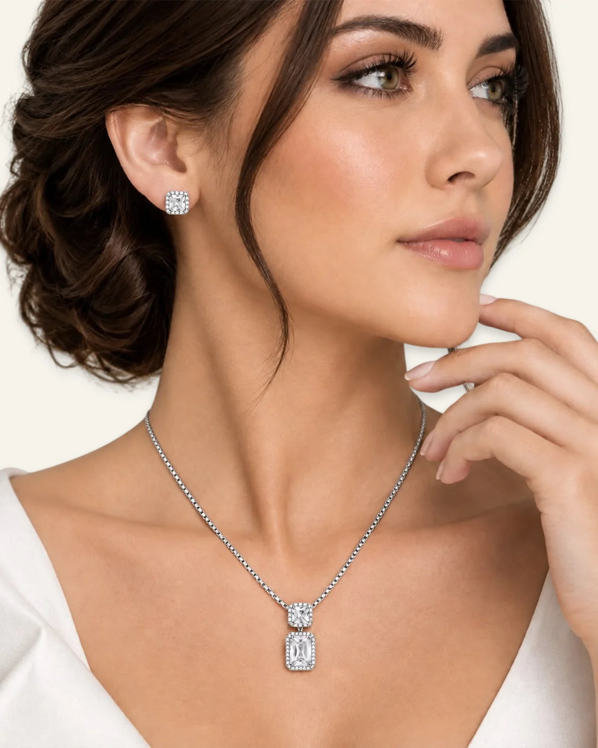 Model wearing the Regalia gemstone jewelry set in clear, featuring an emerald-cut clear stone pendant necklace and matching halo stud earrings.