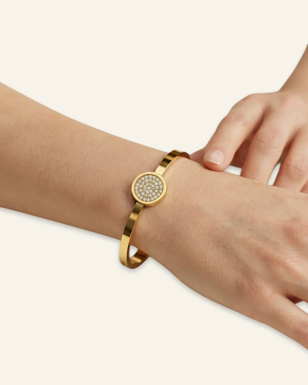 The Celeste Sparkle Bracelet worn on a wrist, featuring a polished gold-tone metal band and a circular centerpiece of shining pave stones against a minimalist neutral background.