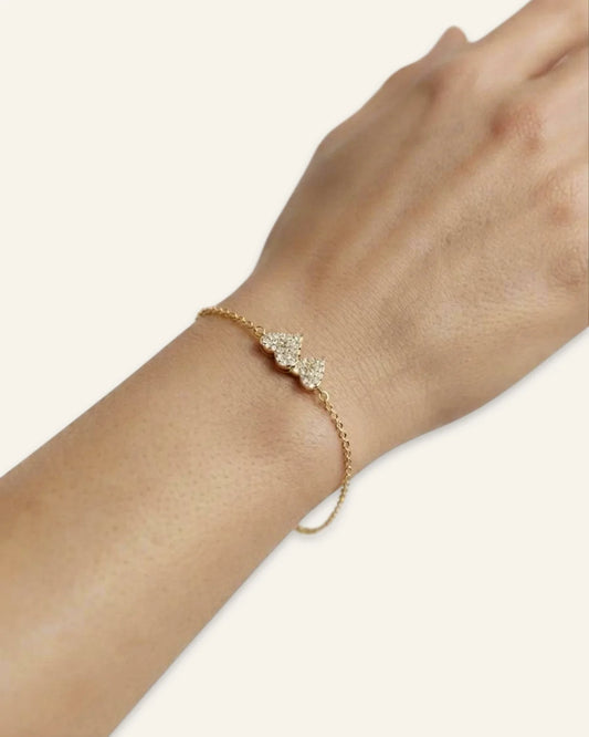 Heart Charm Bracelet, a delicate gold-tone chain bracelet featuring twin interlocking heart charms densely set with shining stones, worn on a wrist displayed on a clean neutral background.