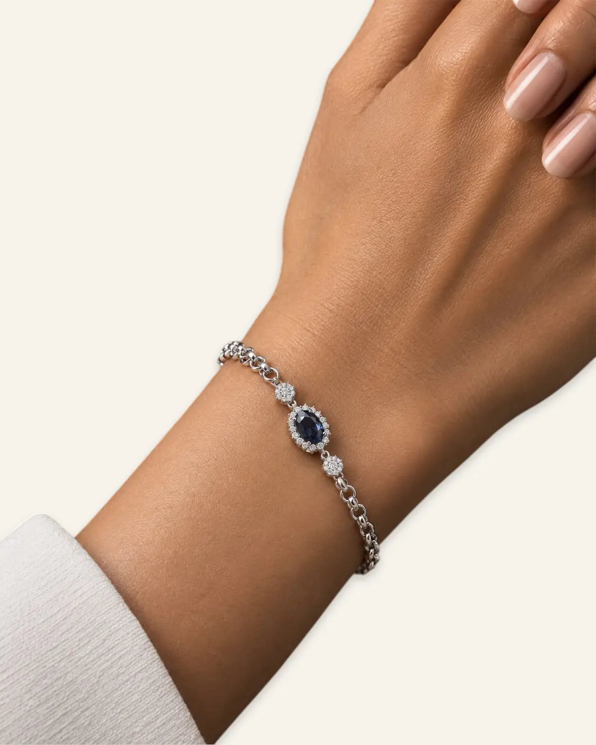 Silver-tone link bracelet featuring a central oval crystal blue stone with a pave halo and delicate crystal accents worn on a model wrist with cream light background.