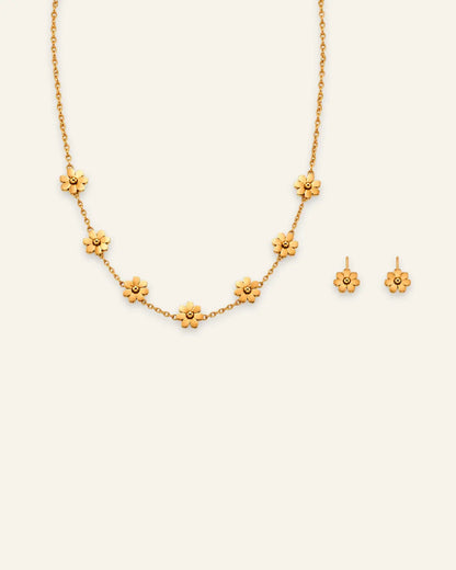 Gold jewelry set featuring a delicate flower station chain necklace and matching small floral stud earrings displayed on a light cream background.