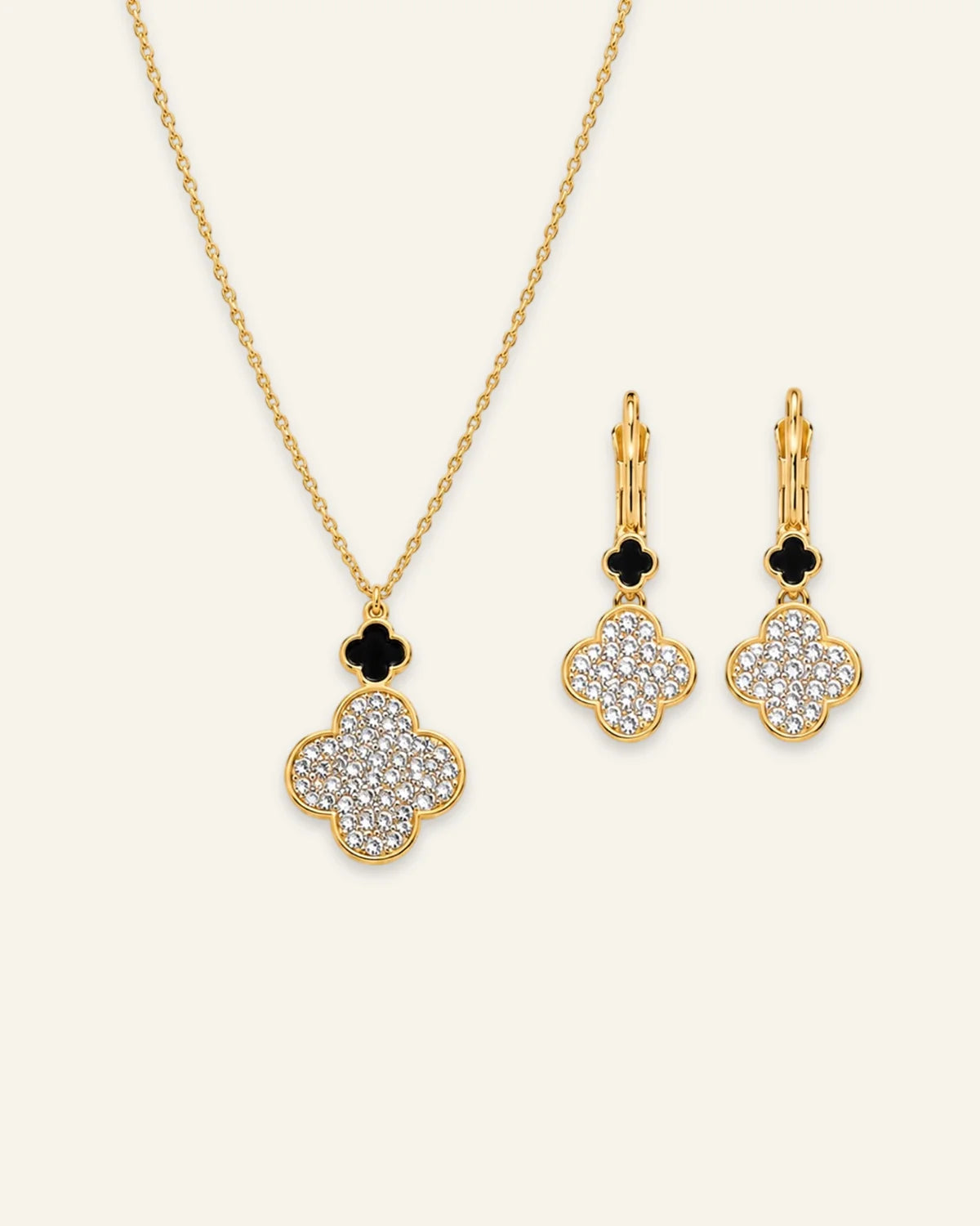 Gold jewelry set featuring a necklace and matching earrings with clover-shaped pendants and floral drop charms, set against a light cream background.