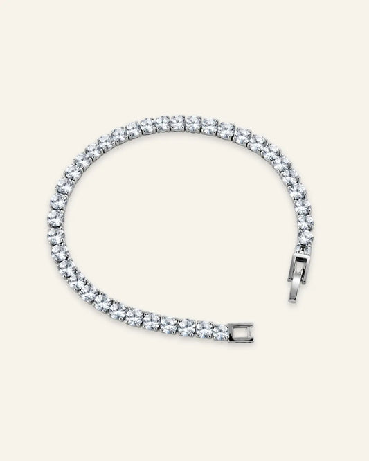 Silver-tone classic tennis bracelet with round brilliant-cut stones in a four-prong setting on a light cream background