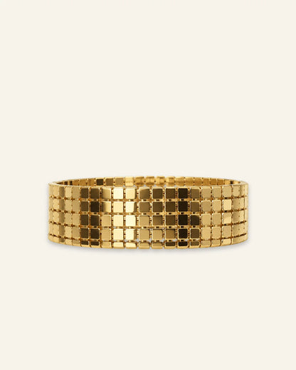 A wide gold bangle bracelet with a grid-like mesh pattern of square links, shown against a light off-white background.