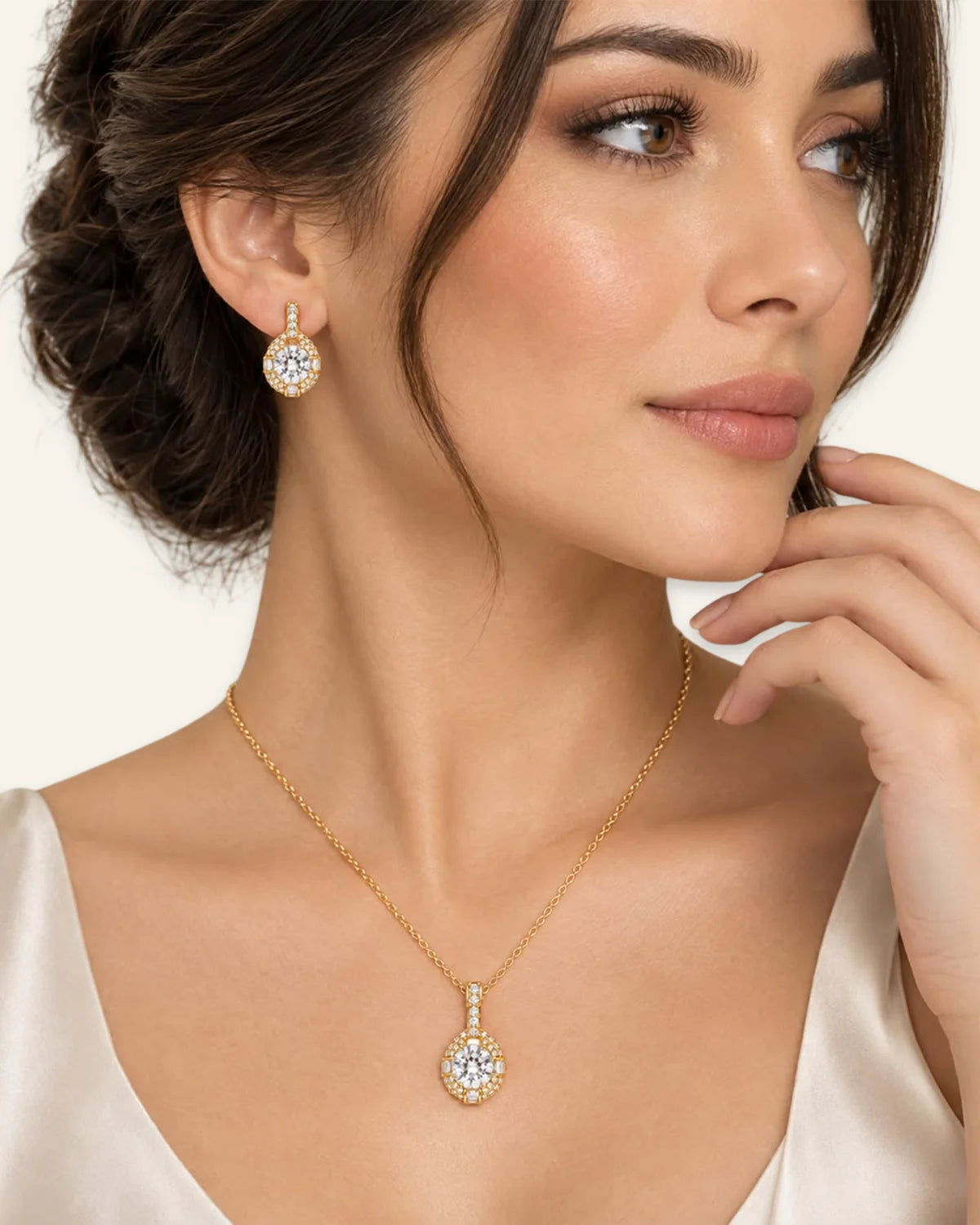 Model wearing a gold halo pendant necklace with a round brilliant clear gemstone and matching gold halo drop earrings.