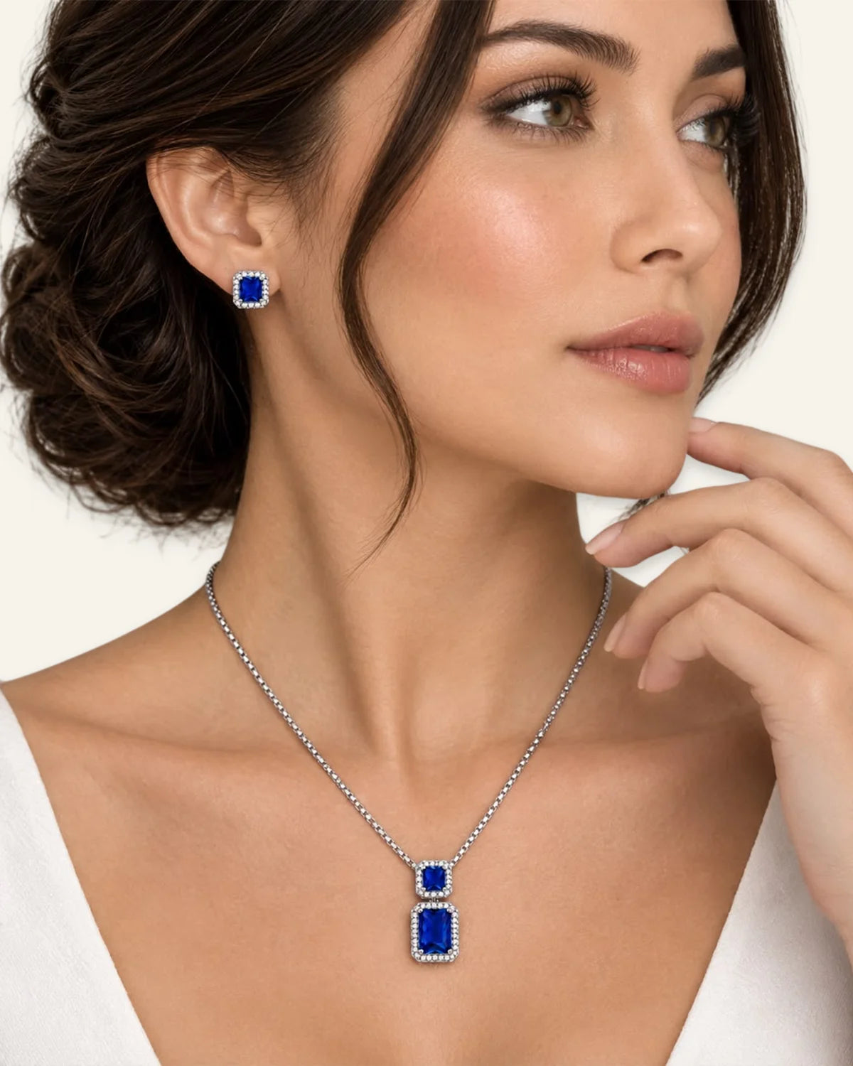 Model wearing the Regalia gemstone jewelry set in blue, featuring an emerald-cut blue gemstone pendant necklace and matching halo stud earrings.