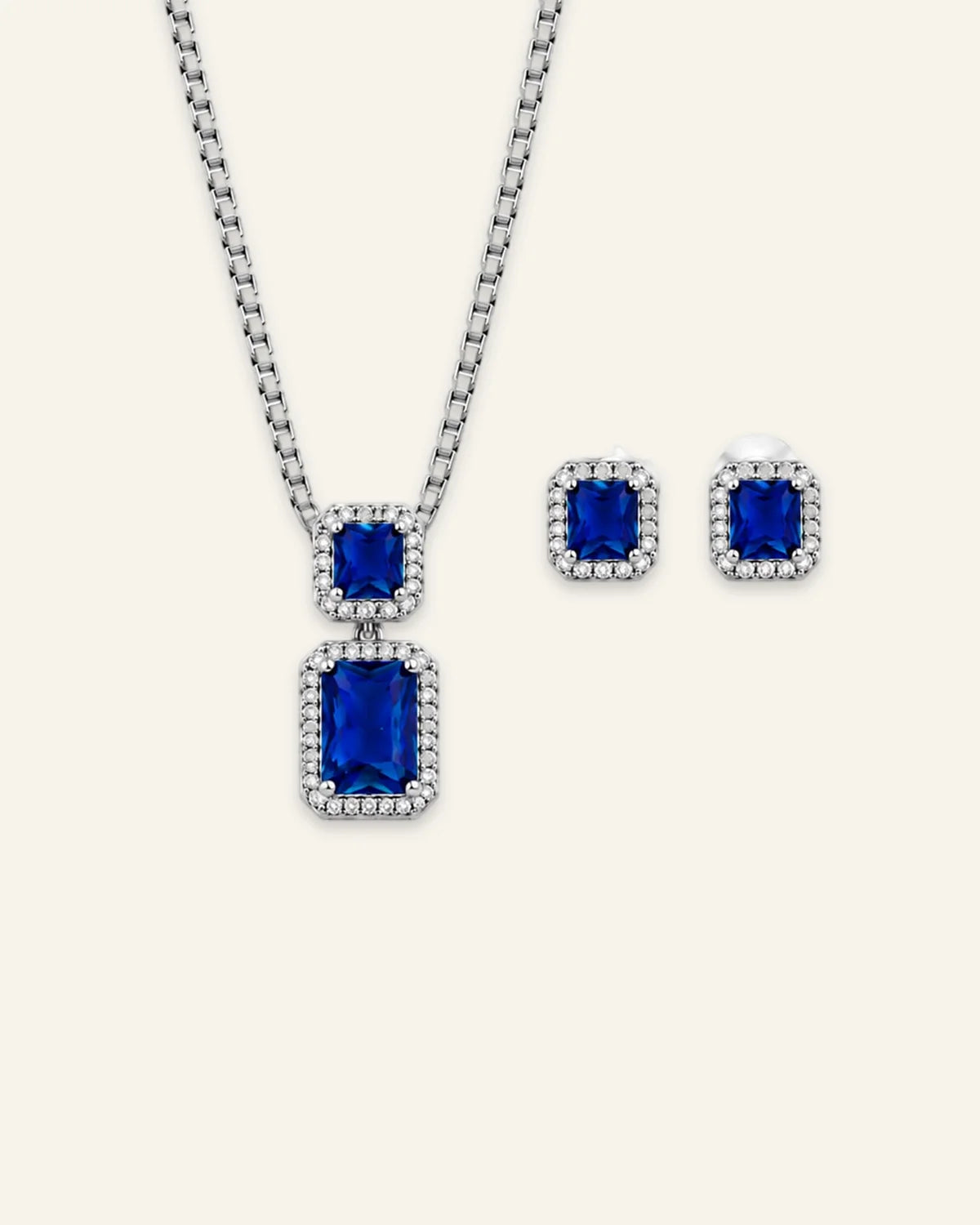 Regalia gemstone jewelry set featuring a silver-tone pendant necklace and matching stud earrings with emerald-cut blue gemstones and clear crystal halos.