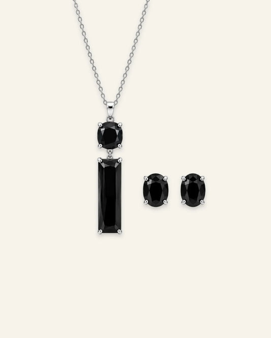 A silver-toned jewelry set featuring a pendant necklace and matching stud earrings with black gemstones, displayed on a light cream background.