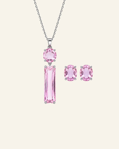 A silver jewelry set featuring a pendant necklace and matching stud earrings with pink gemstones, displayed on a light cream background.