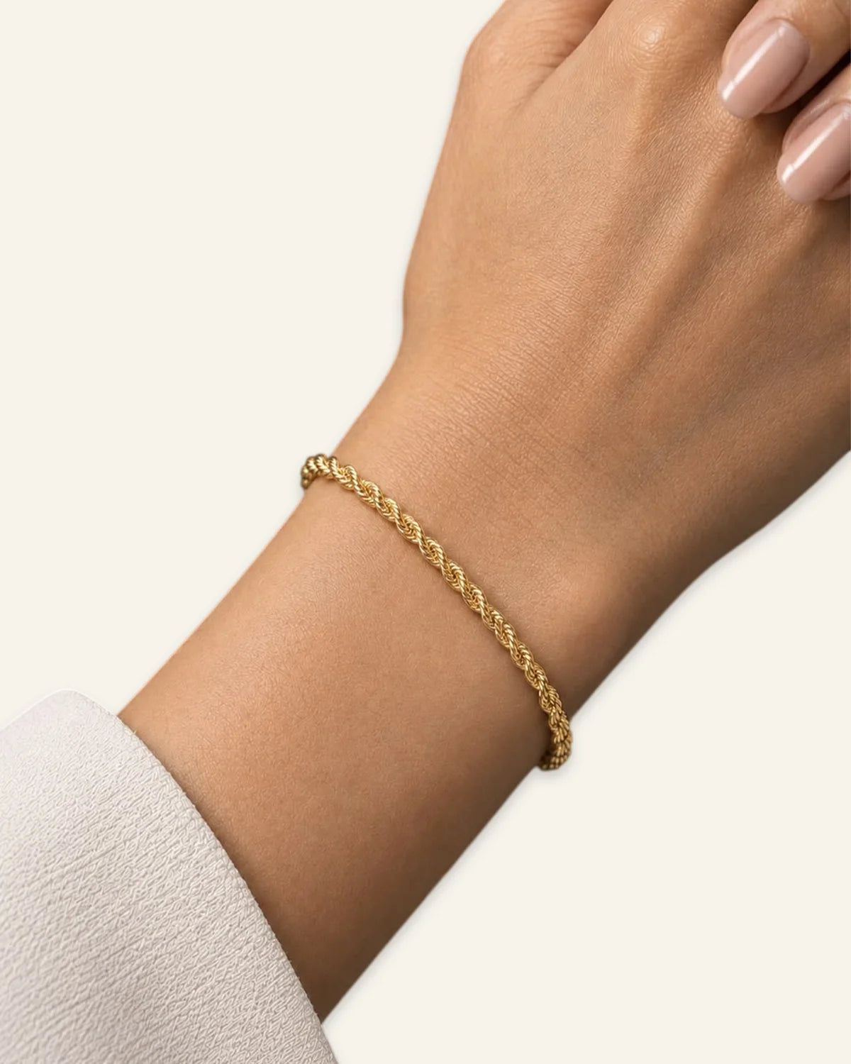 A delicate gold braided cable bracelet worn on a woman's wrist, shown against a clean off-white background.