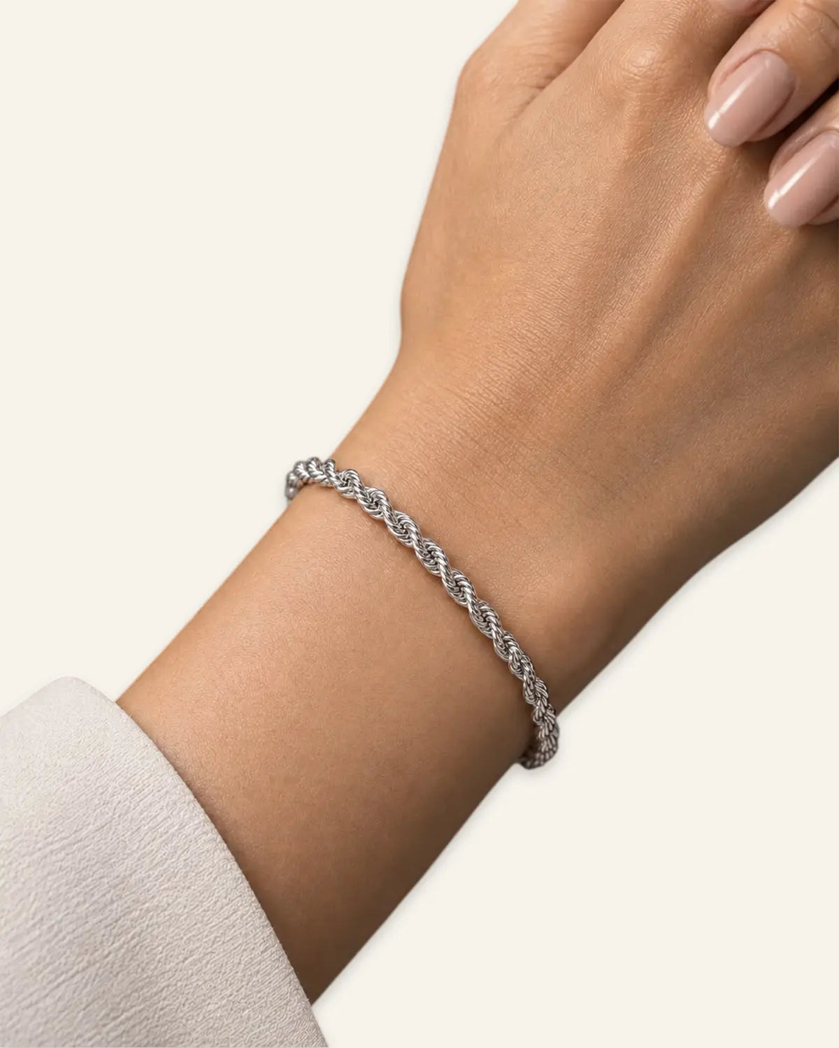 A delicate silver braided cable bracelet worn on a woman's wrist, shown against a clean off-white background.