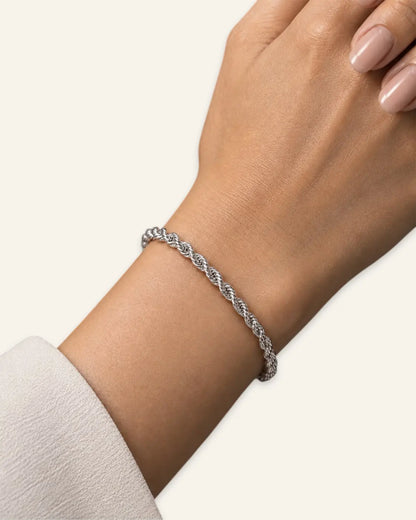 A delicate silver braided cable bracelet worn on a woman's wrist, shown against a clean off-white background.