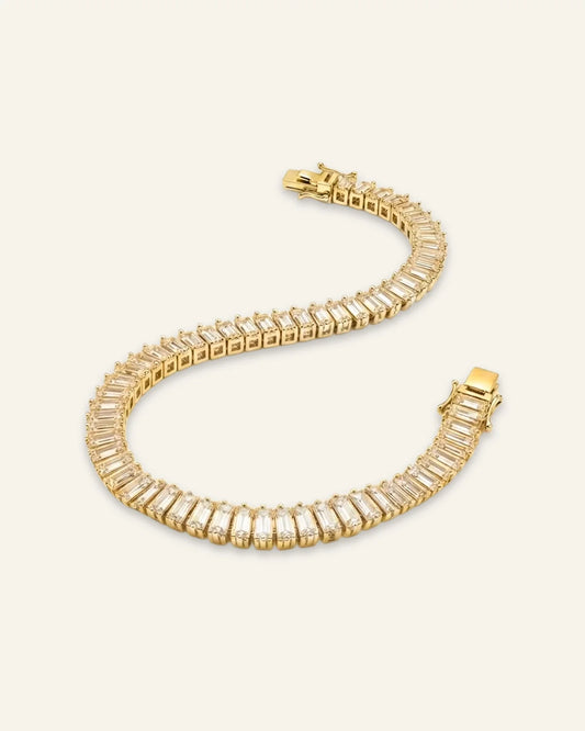 High quality product of a luxury gold-tone dazzling baguette cut tennis bracelet laid out in an S-shape curve, showcasing a continuous stream of rectangular emerald-cut crystal baguette stones and a polished clasp.