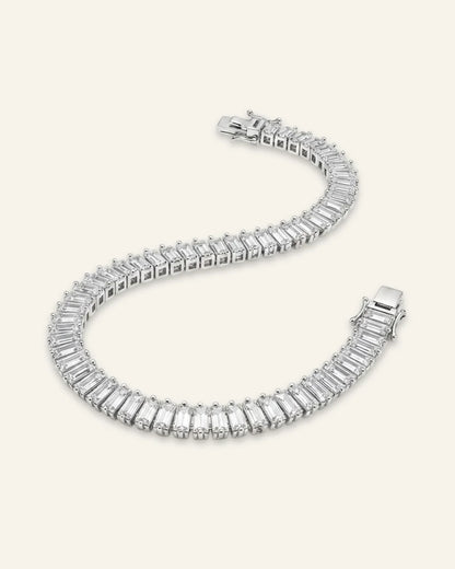 High quality product of a luxury silver-tone dazzling baguette cut tennis bracelet laid out in an S-shape curve, showcasing a continuous stream of rectangular emerald-cut crystal baguette stones and a polished clasp.
