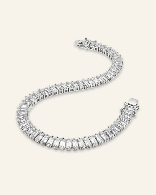 High quality product of a luxury silver-tone dazzling baguette cut tennis bracelet laid out in an S-shape curve, showcasing a continuous stream of rectangular emerald-cut crystal baguette stones and a polished clasp.