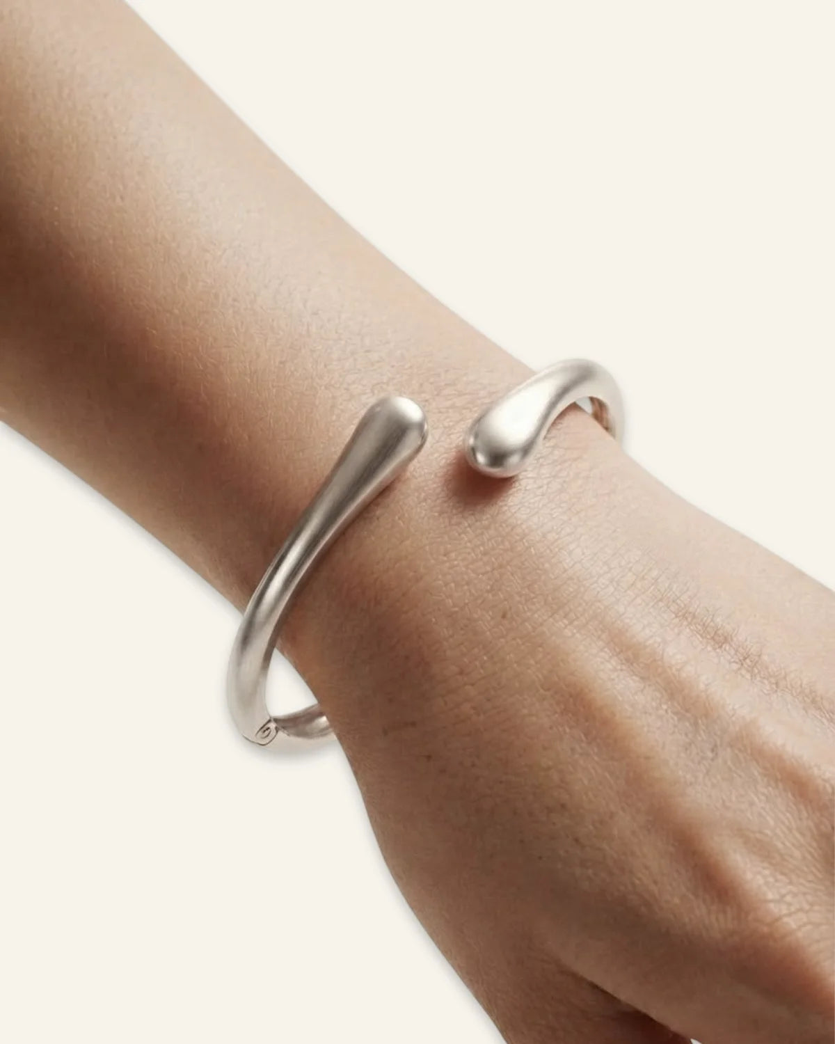 Duo Curve Bracelet, a silver-tone open cuff bracelet with smooth, teardrop-shaped terminals and a hinged closure, worn on a wrist against a neutral background.