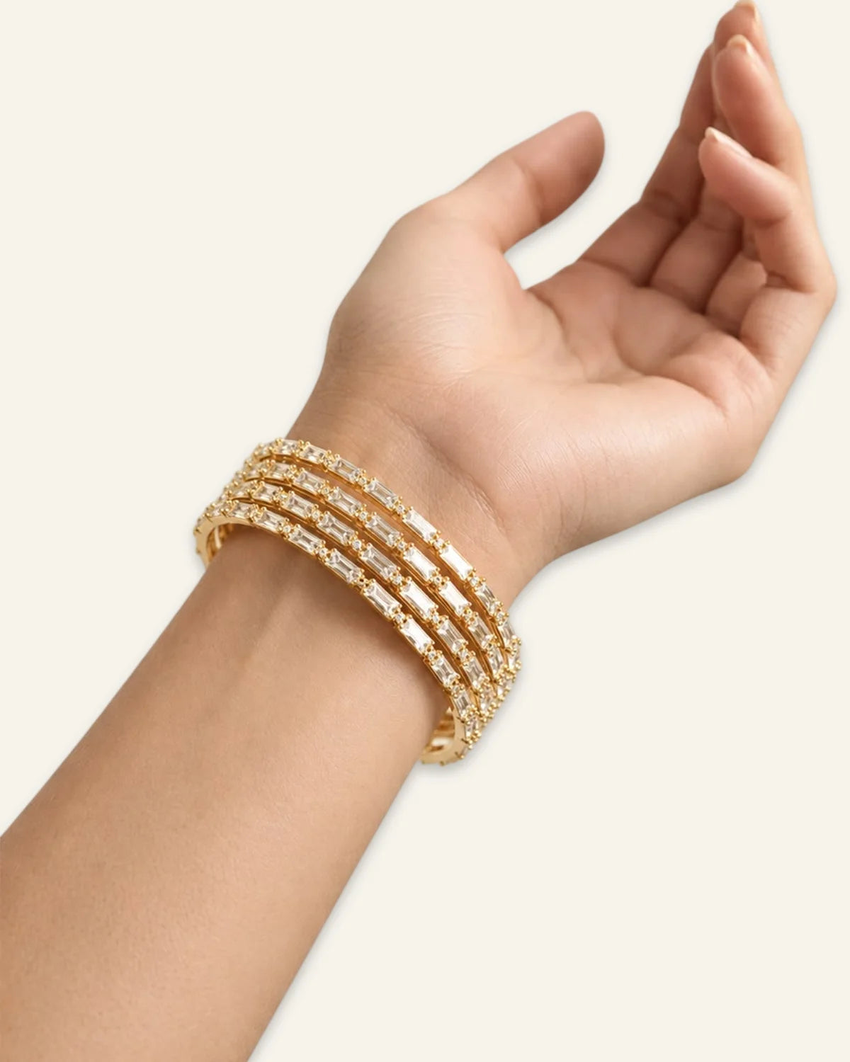Elegant Rhinestone Bracelet, a stacked set of four gold-tone metal bangles densely set with alternating baguette-cut stones and shining stone accents worn on wrist of a hand against a clean neutral background.