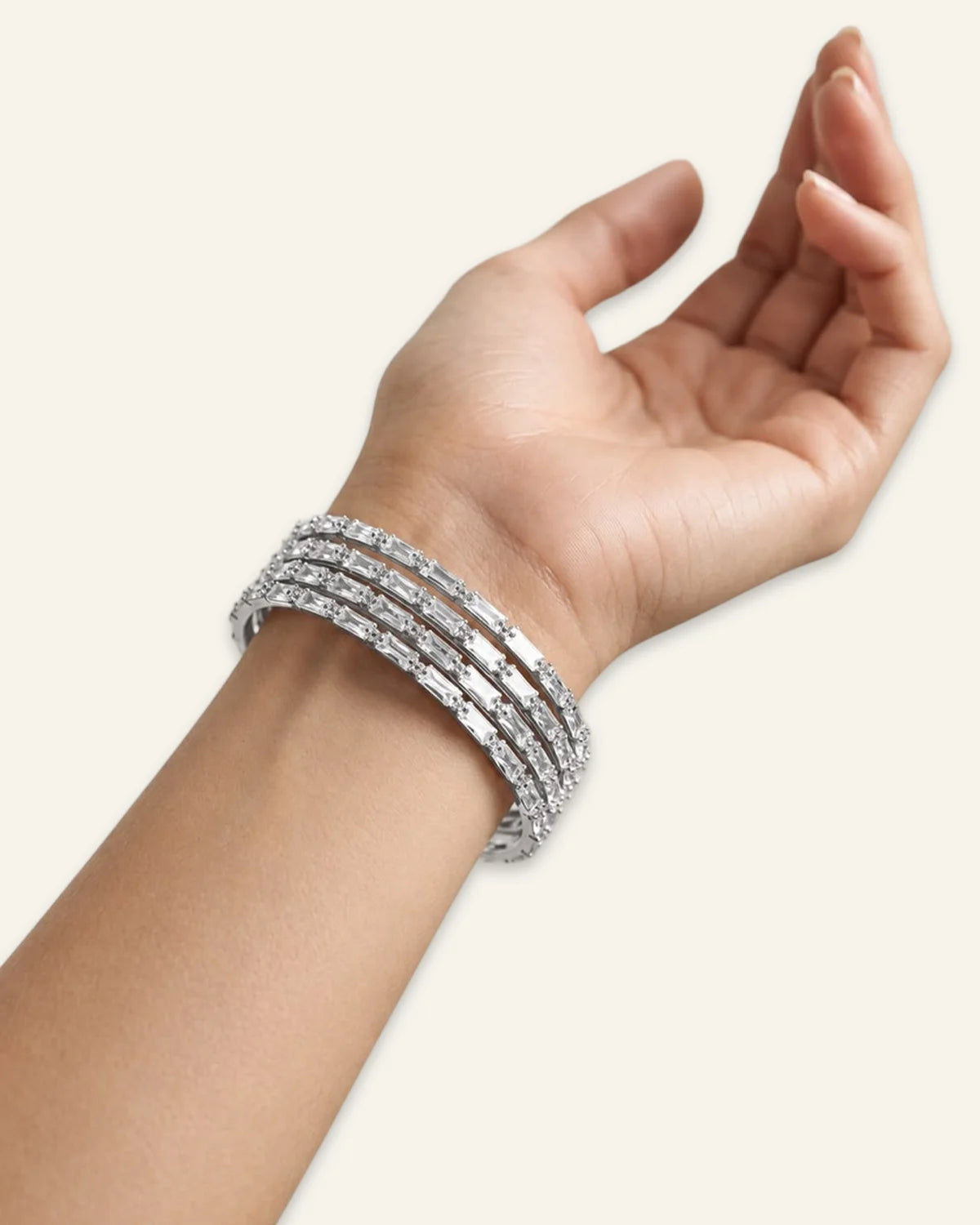 Elegant Rhinestone Bracelet, a stacked set of four silver-tone metal bangles densely set with alternating baguette-cut stones and shining stone accents worn on wrist of a hand against a clean neutral background.