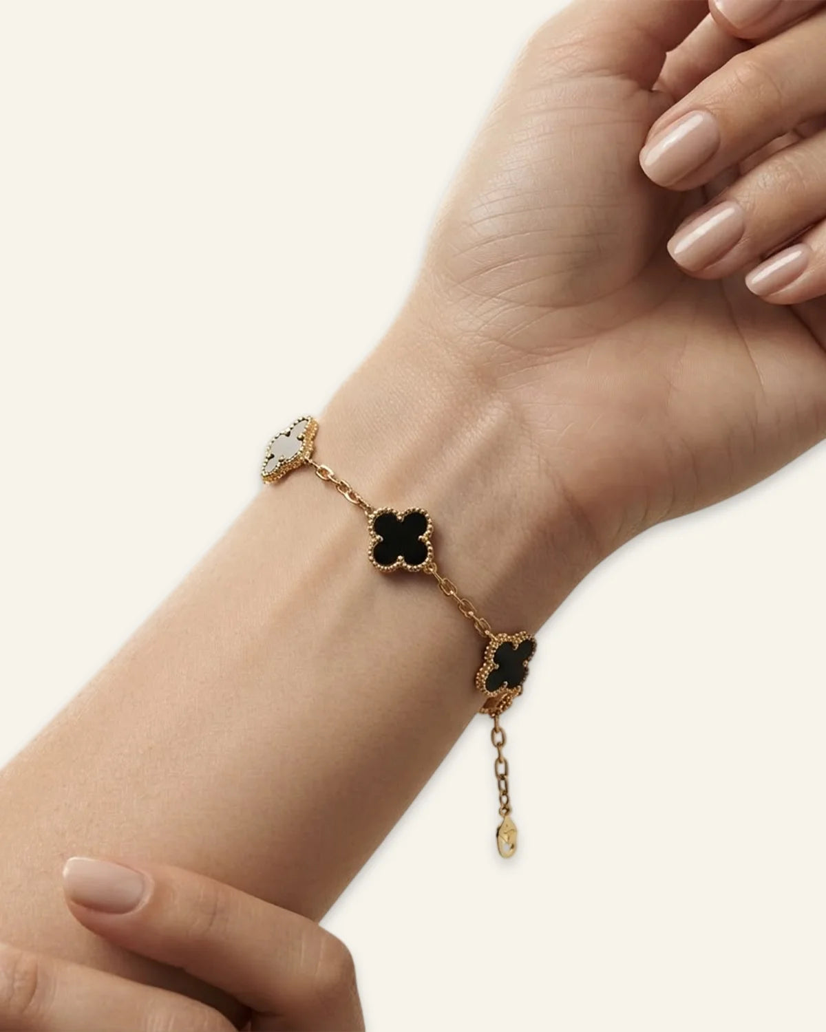 Floral Emblem Bracelet worn on a wrist, featuring textured black leaf clover motifs and beaded borders on a delicate gold-tone chain against a neutral background.