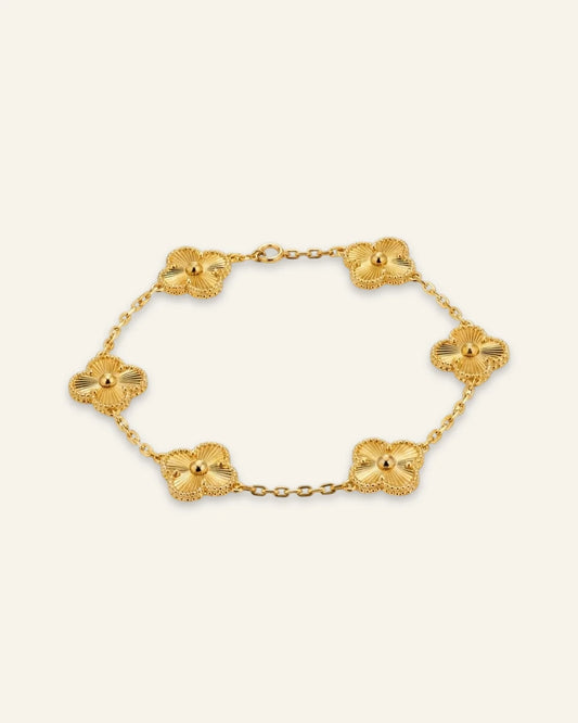 Floral Emblem Bracelet featuring leaf clover motifs with radiating lines and beaded borders on a delicate gold-tone chain against a soft ivory background.