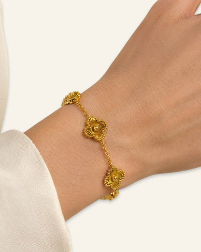 Floral Emblem Bracelet worn on a wrist, featuring textured gold leaf clover motifs with radiating lines and beaded borders on a delicate gold-tone chain against a neutral background.