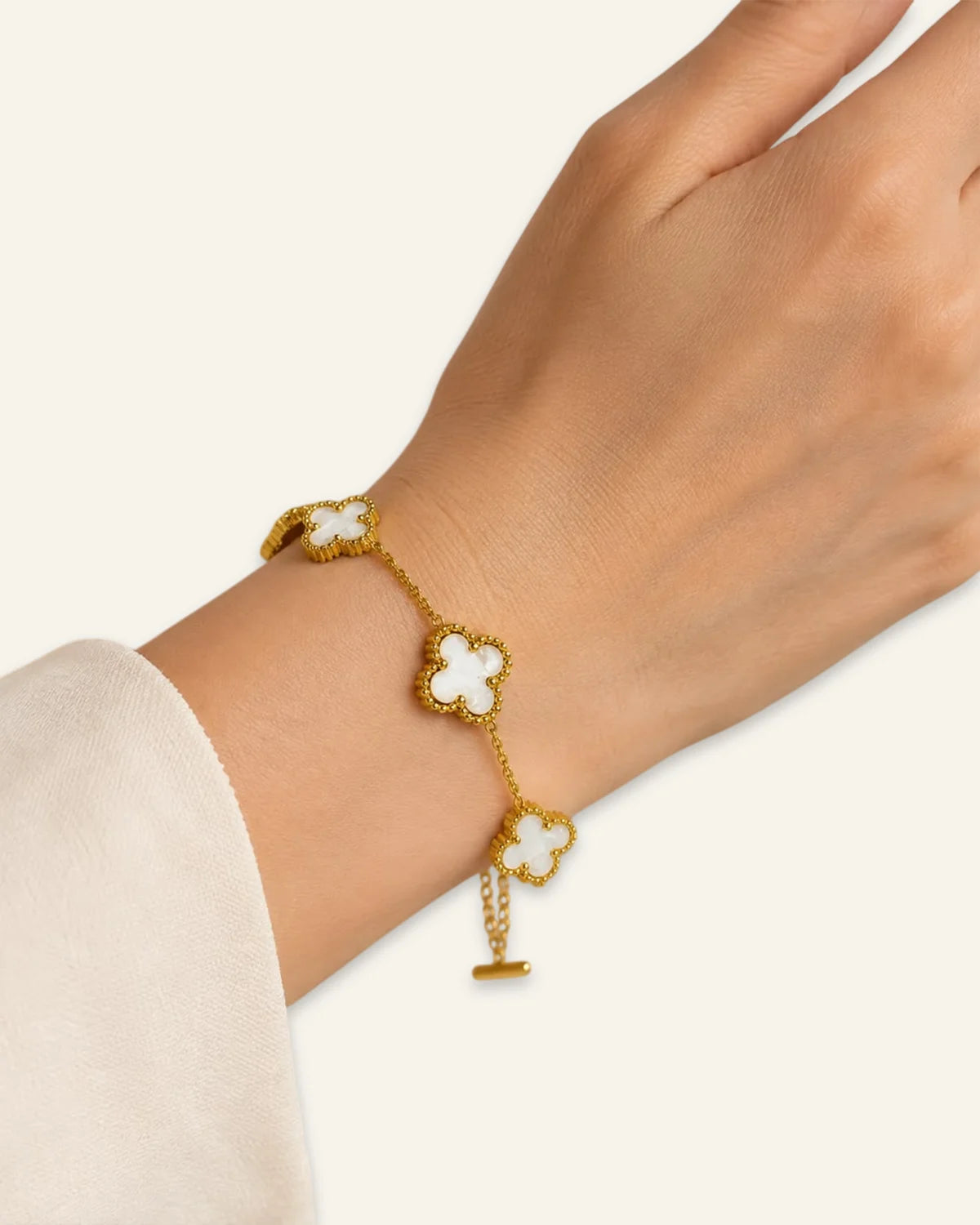 Floral Emblem Bracelet worn on a wrist, featuring textured white leaf clover motifs and beaded borders on a delicate gold-tone chain against a neutral background.