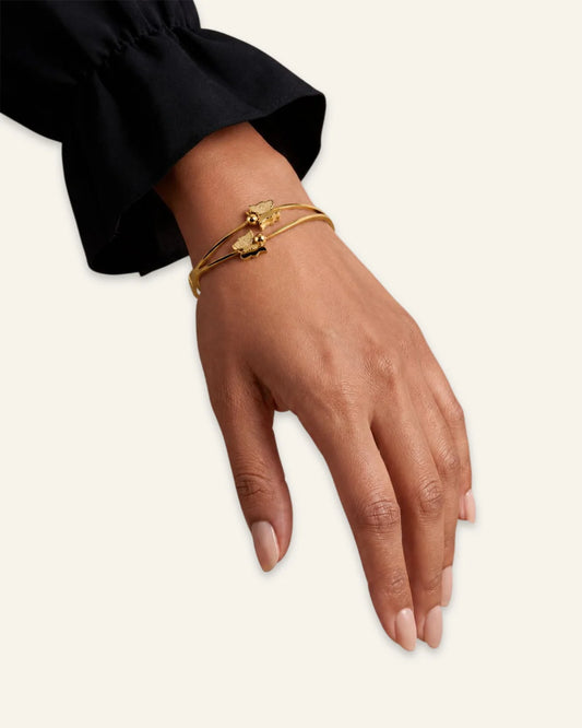 Golden Flutter Butterfly Bracelet, a polished gold-tone double-band hinged bangle featuring two textured butterfly motifs with central spherical accents worn on a wrist of hand against a clean neutral background.