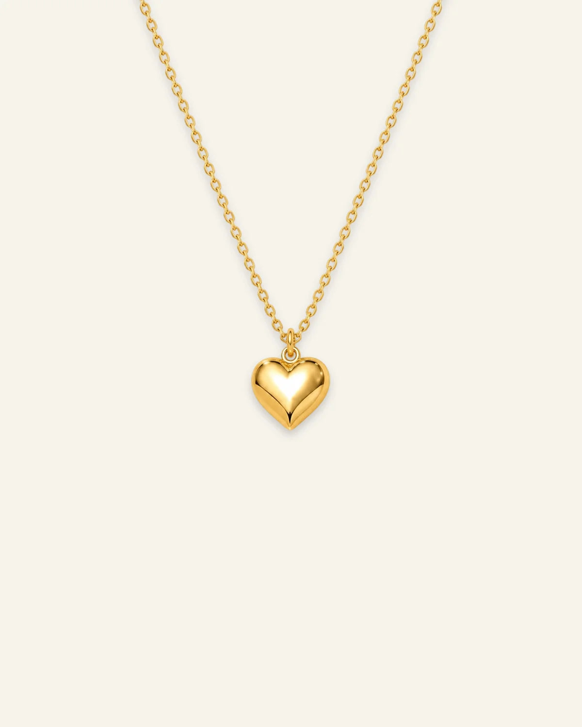 Shiny gold chain pendant necklace featuring a smooth 3D puffed heart pendant on a warm ivory background. 