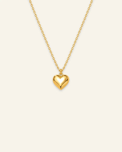 Shiny gold chain pendant necklace featuring a smooth 3D puffed heart pendant on a warm ivory background. 