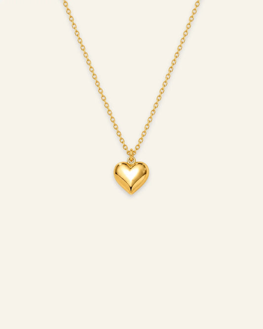 Shiny gold chain pendant necklace featuring a smooth 3D puffed heart pendant on a warm ivory background. 