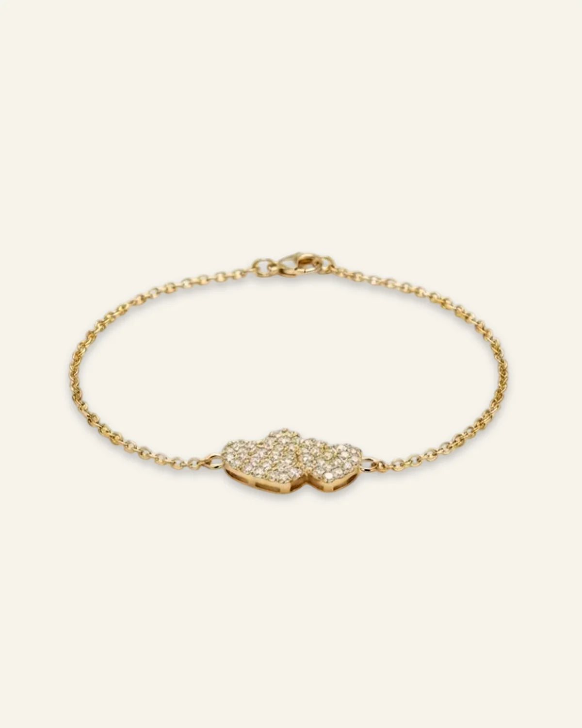 Heart Charm Bracelet, a delicate gold-tone chain bracelet featuring twin interlocking heart charms densely set with shining stones, displayed on a clean neutral background.