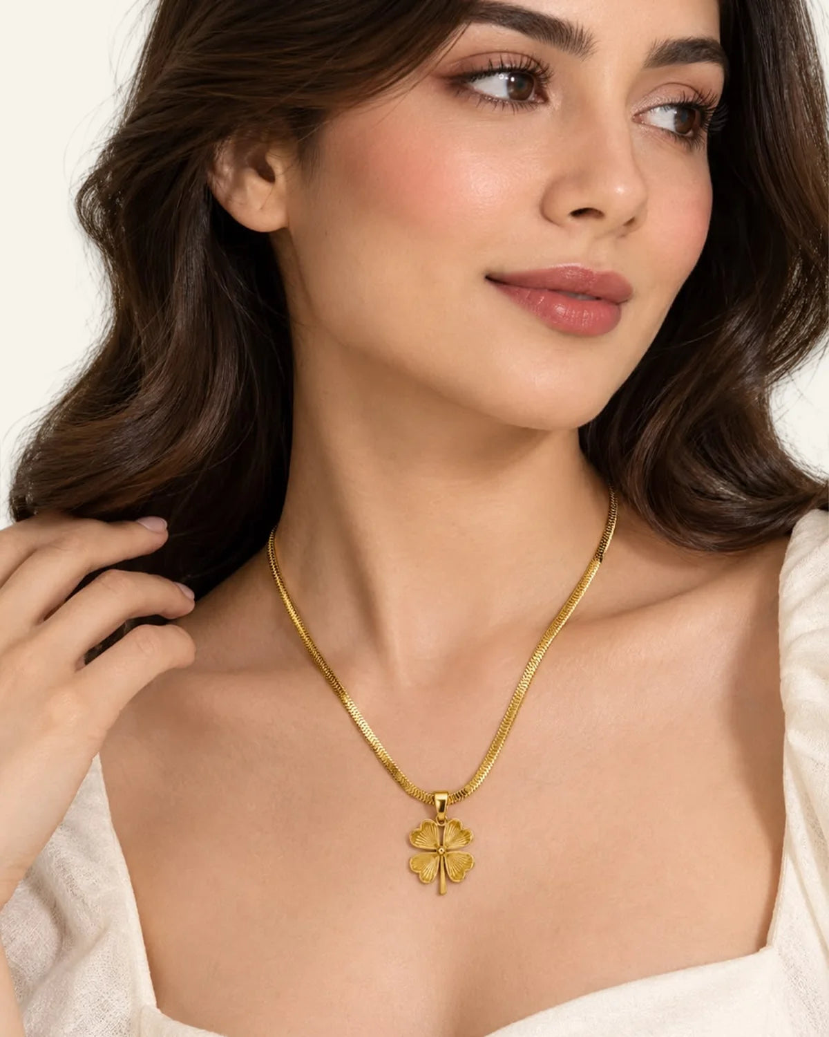 Model wearing a textured gold lucky clover pendant necklace paired with a white top.
