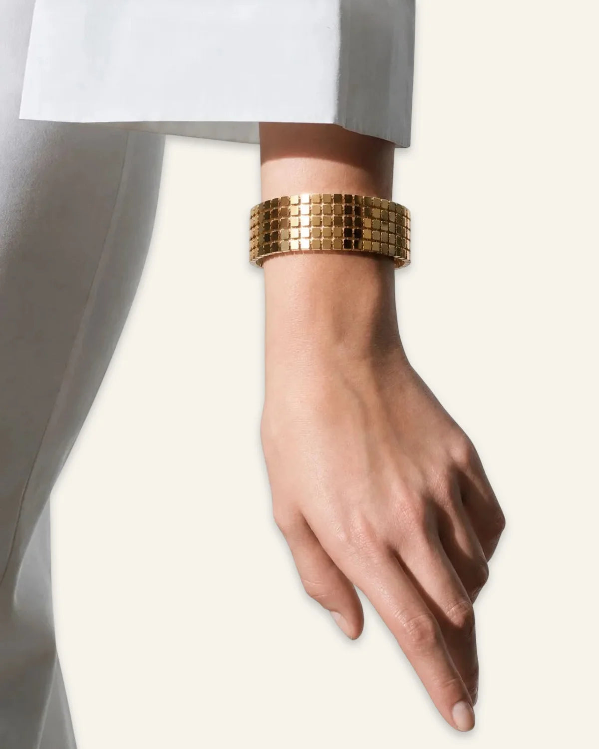 Gold bracelet on a person's wrist against a plain background