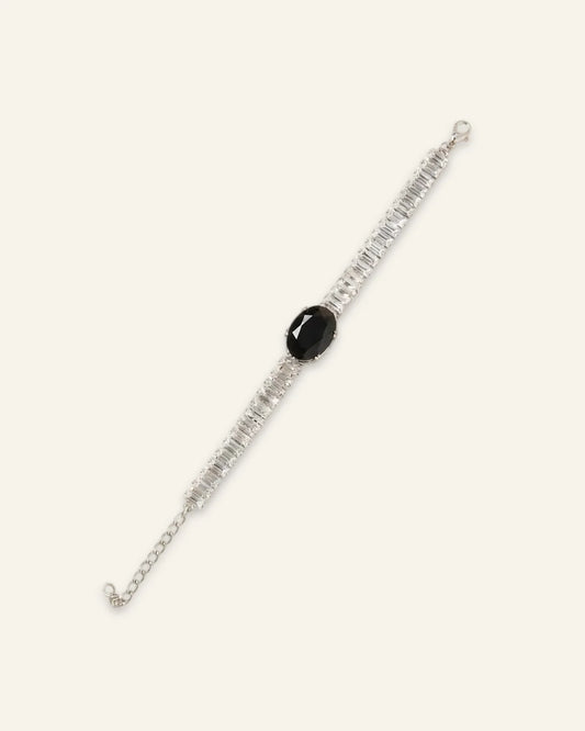 Midnight Luxe Bracelet, a silver-tone crystal line bracelet featuring a large central black oval gemstone flanked by rows of rectangular-cut clear stones and an adjustable chain extension on a neutral background.