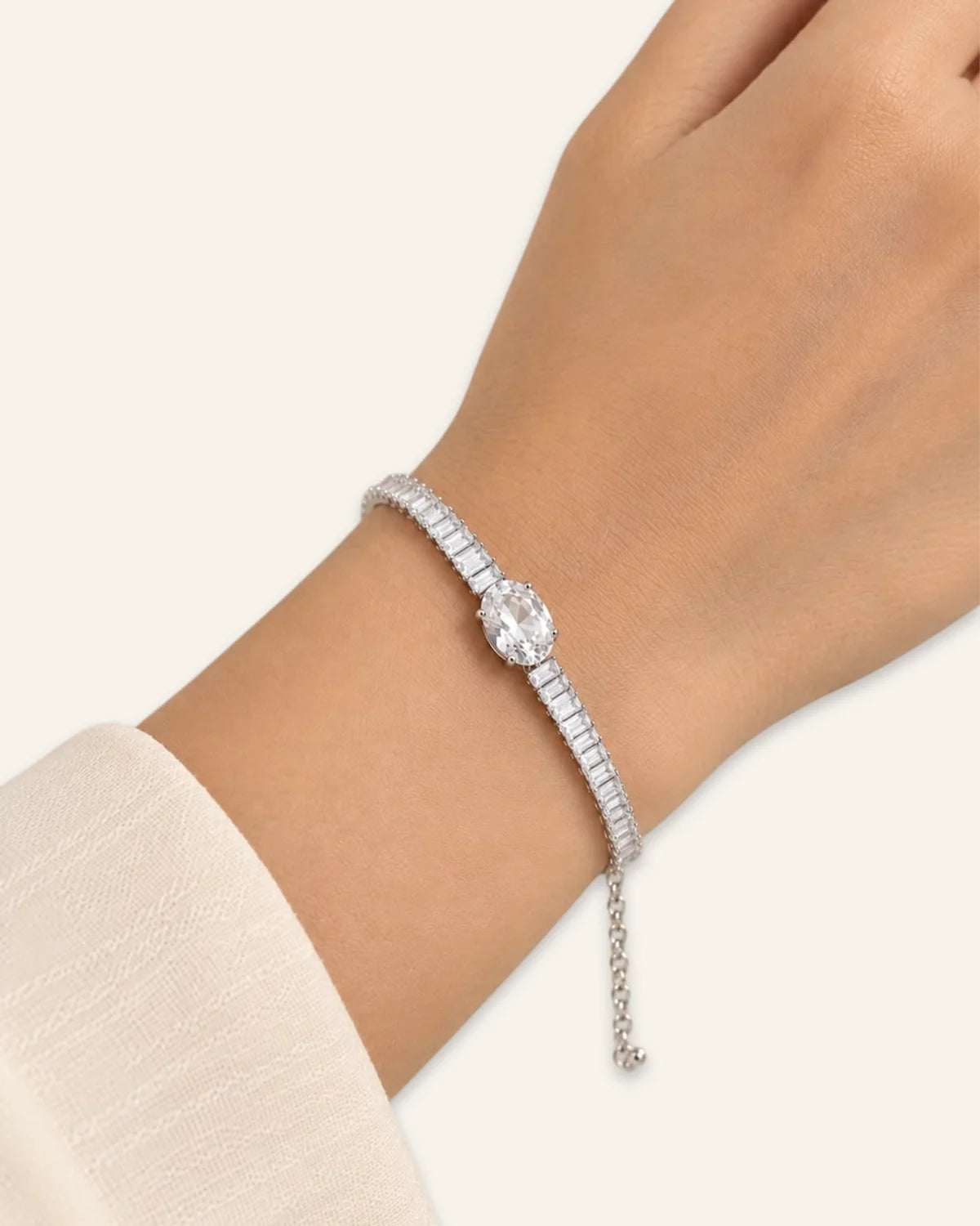 Midnight Luxe Bracelet, a silver-tone crystal line bracelet featuring a large central crystal oval gemstone flanked by rows of rectangular-cut clear stones  and an adjustable chain extension wore on a wrist of a hand on a neutral background.