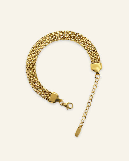 Gold plated stainless steel Milanese mesh bracelet with lobster clasp on light cream background.