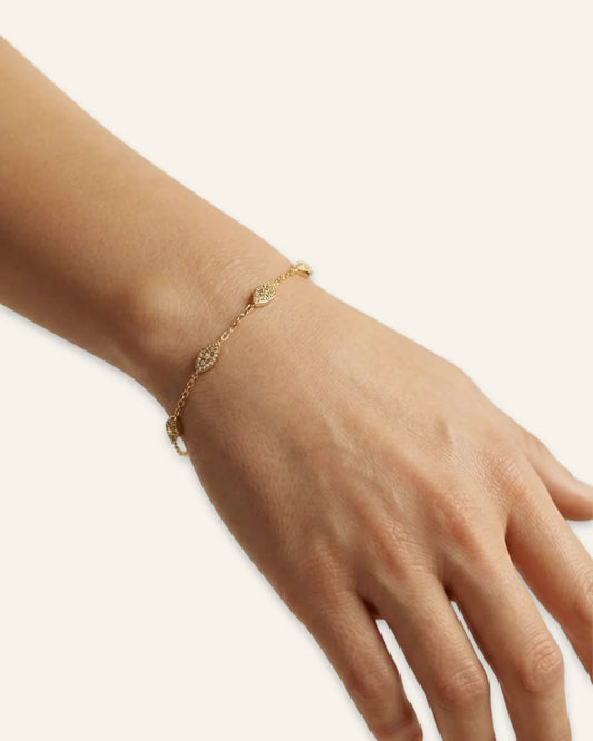 Minimalist Marquise Charm Bracelet, a delicate gold-tone chain bracelet featuring spaced marquise-shaped stations densely set with shining pave stones worn on a wrist of a hand against a clean neutral background.