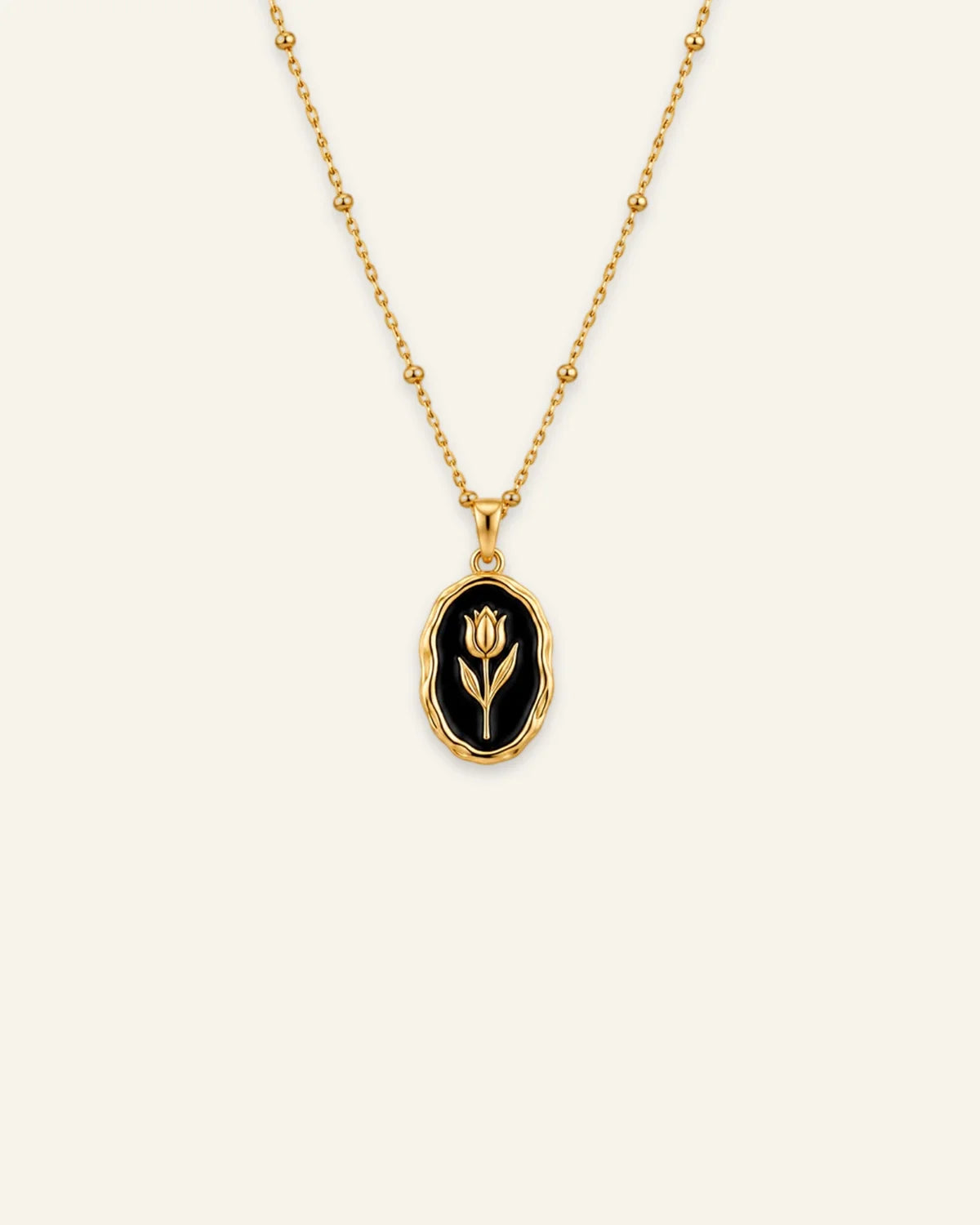 Gold Rose Muse pendant necklace featuring an oval black enamel inlay with a gold flower motif on a beaded satellite chain.