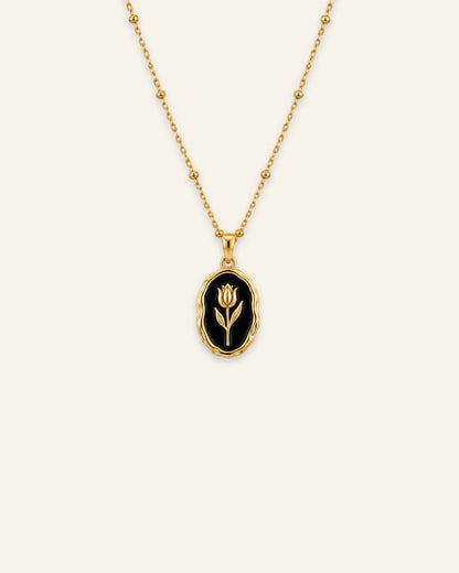 Gold Rose Muse pendant necklace featuring an oval black enamel inlay with a gold flower motif on a beaded satellite chain.