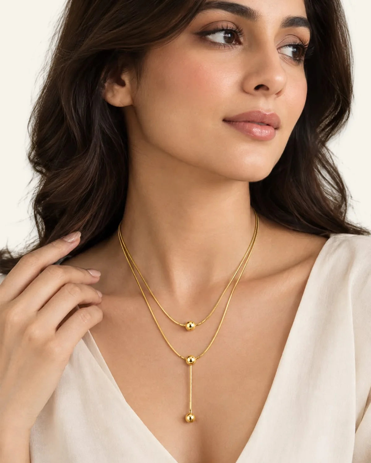 Woman wearing a layered gold triple bead necklace with a lariat drop chain