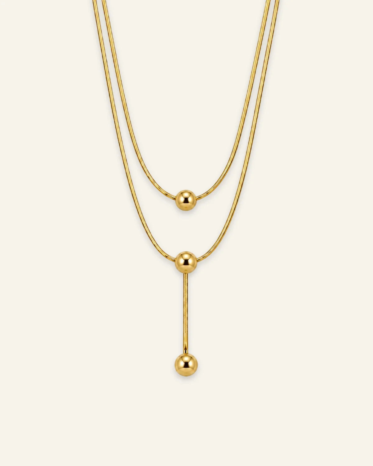 Gold layered necklace featuring three polished sphere beads and a vertical lariat drop chain.