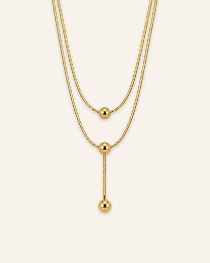 Gold layered necklace featuring three polished sphere beads and a vertical lariat drop chain.
