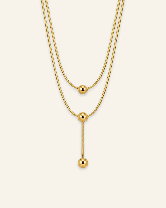Gold layered necklace featuring three polished sphere beads and a vertical lariat drop chain.